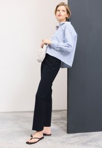Chemise rayée bleu et blanc, coupe ample, associée à un pantalon marine et des tongs noires. Comprend un petit sac tissé blanc.
