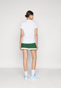 Vit kortärmad t-shirt med en grön plisserad kjol som har en vit rand i fållen, tillsammans med vita strumpor och sneakers med blå detaljer.