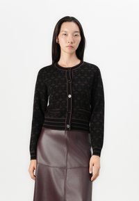 Gilet en tricot noir avec un motif répétitif, col rond et bord contrastant bordeaux ; doté de boutons noirs et de poignets côtelés.