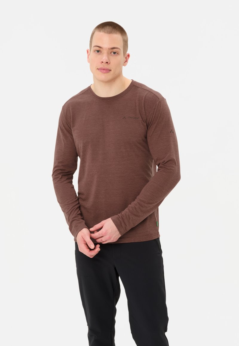 Lange mouwen, bruine t-shirt gemaakt van lichtgewicht stof, met een ronde halslijn en een logo detail op de borst. Gecombineerd met donkere broeken.