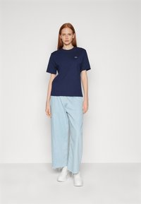 Navy cotton t-shirt with short sleeves and a round neckline, paired with light blue loose-fit denim pants and white sneakers.