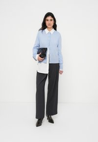 Ανοιχτό μπλε ζακέτα με κουμπιά, λευκό πουκάμισο με γιακά και κάθετες ρίγες, γκρι παντελόνι φαρδύ, και μαύρη τσάντα χειρός. Καφέ μπότες με τακούνι.