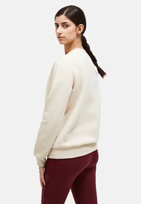 Felpa beige con scollo rotondo e polsini a coste, abbinata a leggings bordeaux. Texture liscia, vestibilità comoda, design minimale.