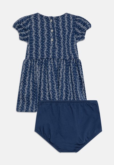 Ναυτικό μπλε βαμβακερό φόρεμα με λευκό λουλουδάτο σχέδιο, φουσκωτά μανίκια, κλείσιμο με κουμπί στο πίσω μέρος και αντίστοιχες σορτς βούλκες. Λείος, απαλός υφασμάτινος ιστός.