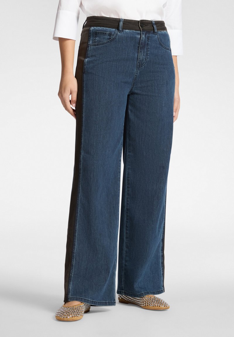 Vaqueros de pierna ancha en denim azul oscuro con un panel lateral negro contrastante. Presentan un diseño clásico de cinco bolsillos y una cinturilla estándar.