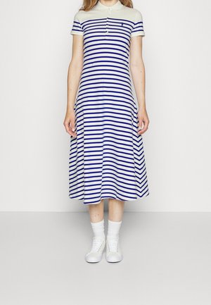 Kvinde iført en hvid og blå horisontalt stribet midi-kjole med krave, korte ærmer, hvide sokker og hvide sneakers.