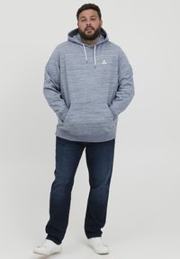 Blå melert bomull hettegenser med frontlomme og snorhette, kombinert med mørkeblå jeans og hvite joggesko.