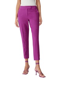 Pantalon ajusté longueur cheville en violet vif, avec une texture lisse et une coupe sur mesure. Associé à des talons à brides assortis.