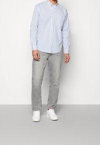 Lichtblauw en wit gestreept overhemd met knopen, lange mouwen, gecombineerd met grijze jeans en witte sneakers. Eenvoudig kraagontwerp, zonder zichtbare patronen.