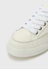 Weiße Ledersneaker mit dicker Gummisohle, runder Zehenform und flachen weißen Schnürsenkeln. Auffällige Nähte und Ösenakzente.
