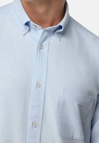 Ljusblå skjorta i texturerat tyg med krage, knappslå fram och en bröstficka.