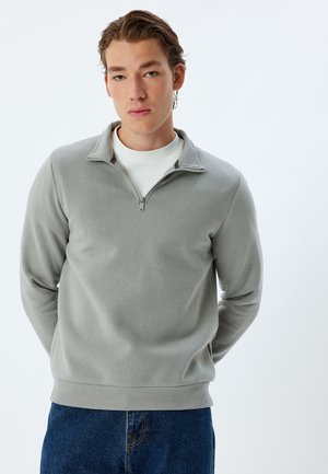Light gray quarter-zip sweatshirt made of soft fabric, featuring a ribbed hem and long sleeves, paired with blue jeans.