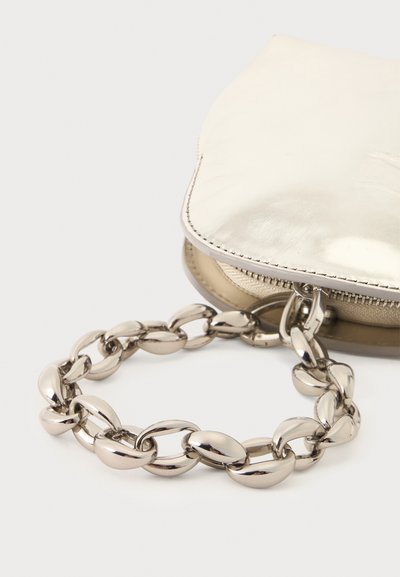 Anse en chaîne argentée brillante fixée à un petit sac à main métallique beige avec une fermeture éclair sur une surface blanche.