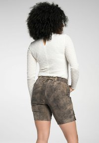 Langärmliges weißes Oberteil aus strukturiertem Stoff mit Schlitz auf der Rückseite, kombiniert mit braunen Wildledershorts mit Knöpfen und verstellbarem Bund.