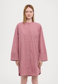 Abito camicia a maniche lunghe e colletto in rosa pallido. Presenta una chiusura con bottoni, taschino sul petto e un sottile dettaglio ricamato. Tessuto dalla texture liscia.