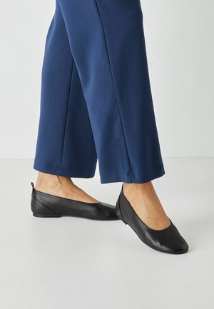 Czarne skórzane baleriny na niskim, zaokrąglonym obcasie, z gładką cholewką i subtelnym przeszyciem wzdłuż krawędzi, dodającym detalu.