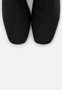 Calzado negro y elegante con diseño de punta y costuras visibles. Fabricado con un material liso y mate que presenta una estética minimalista.