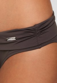 Parte inferiore di bikini grigia scura con cintura arricciata e accento logo argentato. Il materiale è liscio e elasticizzato, con bordi cuciti.