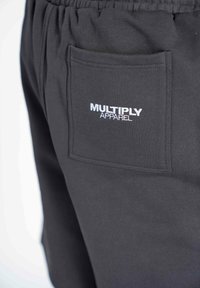 Pantalones cortos de algodón negros con cintura elástica, con un bolsillo de parche y el logotipo bordado en blanco "MULTIPLY APPAREL". Textura suave.