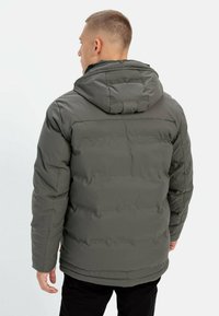 Polstret jakke i mørkegrøn med hætte, der har et quiltet design og en subtil glans. Inkluderer elastiske manchetter og en taljelængde.