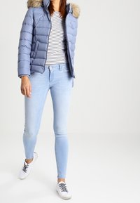 Ljusblå puffjacka med pälsfodrad huva, randig långärmad tröja, ljusblå smala jeans och vita sneakers med svarta snören.