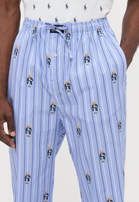 Blauwe gestreepte broek met een klein geborduurd teddybeerontwerp in een blauwe outfit. Relaxte pasvorm met een elastische tailleband en koord.