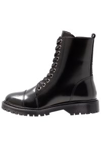 Bota de combate de cuero negro con cordones, suela gruesa, ojales de metal y una lengüeta en la parte trasera.