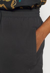 Svarta träningsshorts i lättviktsmaterial, med elastiskt midjeband, sidofickor och en diskret logodetalj vid fållen.