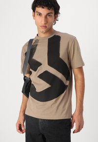 Short-sleeve beige t-shirt made of cotton, featuring a large black graphic design on the front, round neckline, and regular fit.