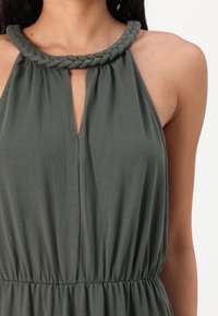 Vestido verde com decote halter, abertura em forma de olho-chave e cintura franzida, apresentando uma textura de tecido suave e lisa.