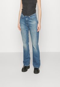 Jeans a zampa d'elefante in denim blu, con un lavaggio sbiadito, design a cinque tasche e chiusura con zip. Abbinati a stivali neri con plateau.