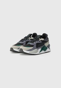 Sportliche Sneakers aus einer Mischung von schwarzen, grauen und grünen Materialien, strukturierten Mesh-Einsätzen und einer klobigen weißen Sohle mit kantigen Akzenten.