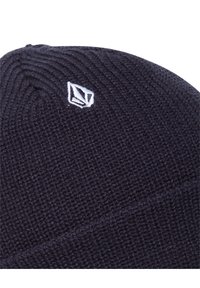 Close-up of a dark knitted beanie with a small white geometric logo embroidered near the top.