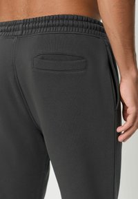 Dunkelgraue Jogginghosen aus weichem Stoff, mit einem elastischen Bund und einer einzigen Gesäßtasche mit horizontaler Öffnung.