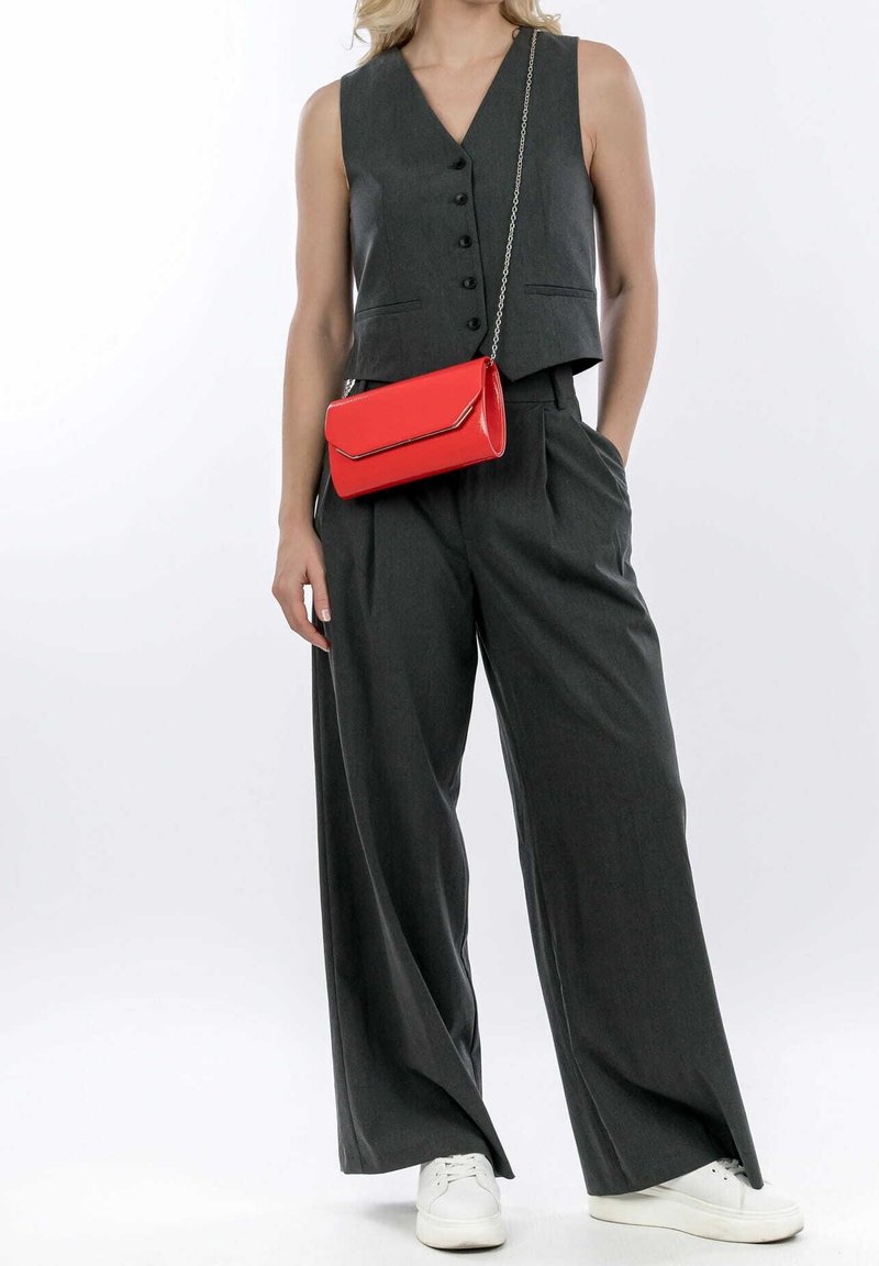 Chaleco gris sin mangas con botones, combinado con pantalones anchos grises y zapatillas blancas. Un bolso rojo con cadena completa el look.