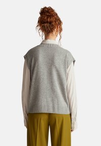 Grau gestrickte Weste mit kurzen Ärmeln und geripptem Saum, getragen über einem leicht gestreiften Hemd und olivgrünen Hosen. Strukturiertes Wollmaterial.