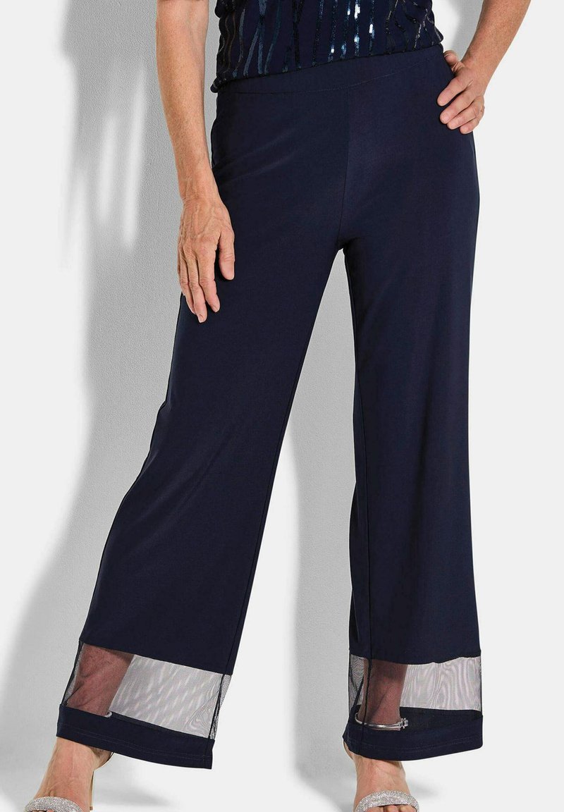 Marineblauwe wijde broek van zacht materiaal, met doorzichtige mesh accenten aan de zoom en een elastische tailleband voor comfort.