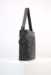 Zwarte leren schoudertas met een getextureerd voorpaneel en een verstelbare band met meerdere metalen oogjes en een gesp, die op een witte ondergrond staat.