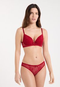 Czerwony koronkowy biustonosz i pasujące majtki z karbowanymi krawędziami, z kwiatowym wzorem, regulowanymi ramiączkami i kokardką na środku.