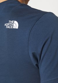 Camiseta de manga corta azul marino hecha de una tela suave, con un logo blanco en el hombro izquierdo y detalles de costura mínimos.