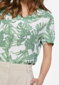 Blusa a maniche corte con scollo a V, caratterizzata da uno sfondo bianco con motivi di foglie verdi; tessuto leggero con vestibilità comoda.