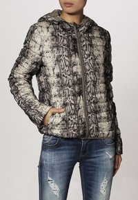 Vadderad jacka med ett mönster av faux ormskinn i nyanser av grått och beige. Har huva, dragkedja fram och sidofickor. Bärs med blå jeans.