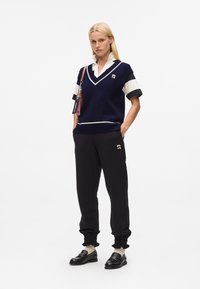 Navy knitted sweater with white trim, black jogger pants, and black loafers. The outfit features a layered, collared shirt beneath.