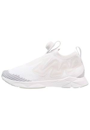 Białe sportowe buty wsuwane z szarymi akcentami na palcach, falistym wzorem po bokach, pętelkami na języku i pięcie oraz grubą teksturowaną podeszwą.