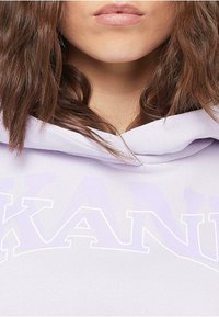 Lila Hoodie mit einem großen, weißen grafischen Textdesign. Weiches Material mit lockerer Passform und verstellbarem Kordelzugkapuze.