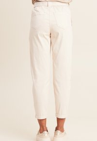 Witte katoenen broek met een relaxed fit, met opgerolde boorden, elastische tailleband en twee achterzakken. G gedragen met lichtgekleurde sneakers.