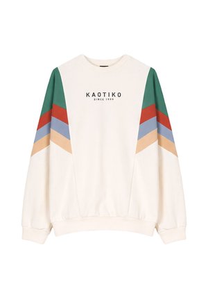 Hvit genser med grønne, røde, blå og beige chevronstriper på ermene og teksten "KAOTIKO SINCE 1999" på brystet.