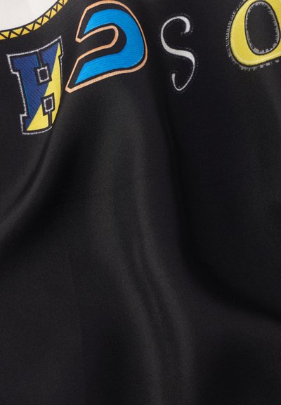 Juoda medžiaga su spalvingais įvairių stilių išsiuvinėtais raidėmis: geltonomis, mėlynomis ir baltomis, su lygiu paviršiumi ir šiek tiek blizgesio.