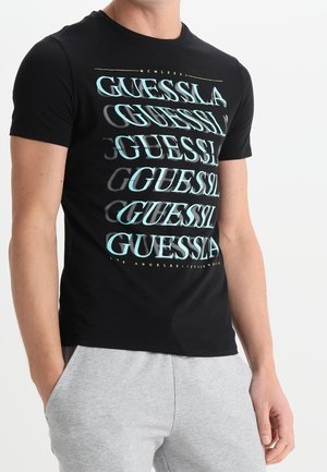 T-shirt noir avec le texte répété « GUESS » en turquoise et gris. Col rond, manches courtes, fabriqué en tissu doux mélangé de coton.