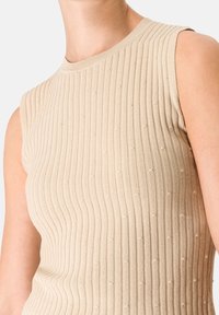 Béžový žebrovaný pletený top bez rukávů s texturovaným vzorem a malými vyvýšenými body, s kulatým výstřihem a tailored střihem.
